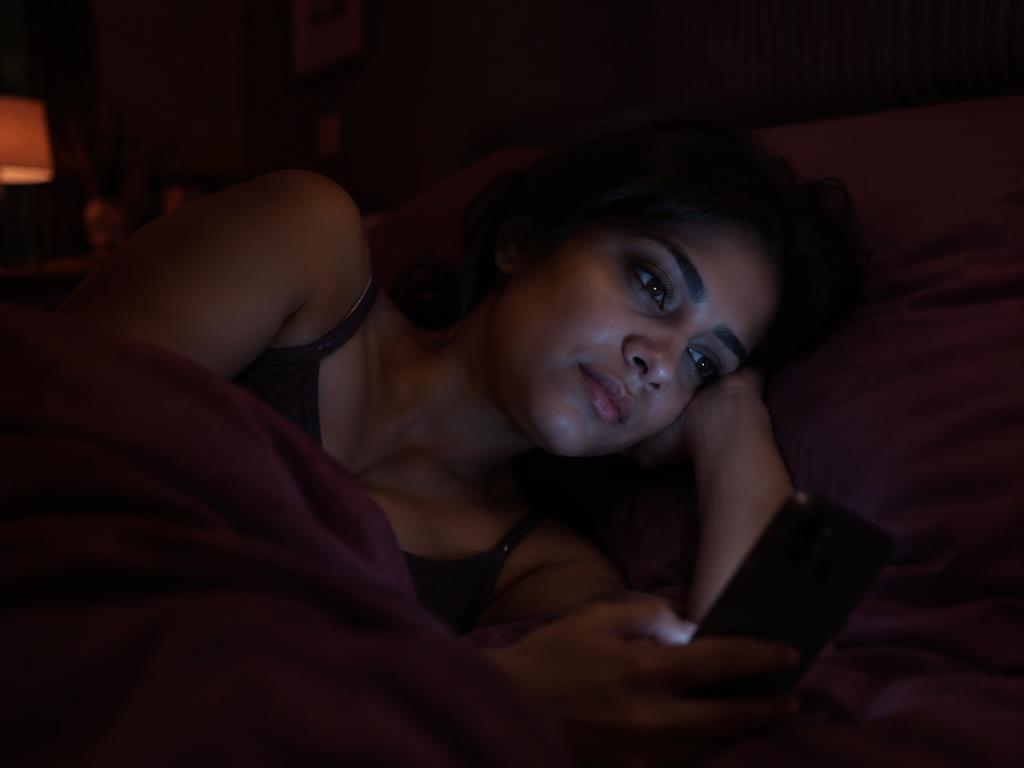 A woman lying awake in bed at 2 AM, lit by her phone, overthinking